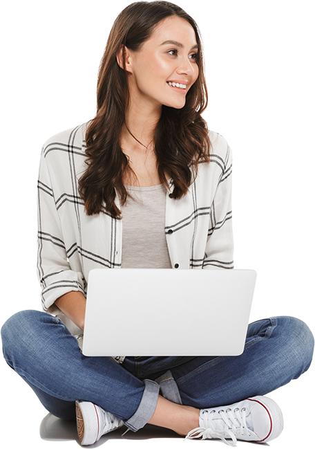 Smiling Young Woman Sitting Cross-Legged On The Floor, Wearing A Casual Plaid Shirt, Jeans, And Sneakers, Holding A Laptop On Her Lap And Looking To The Side